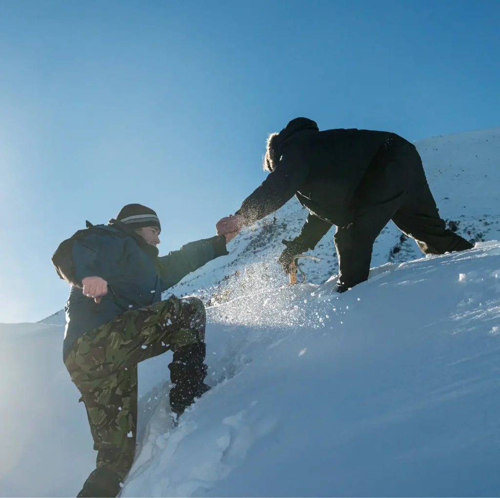 A man helping another man climb up a snowy hill Image