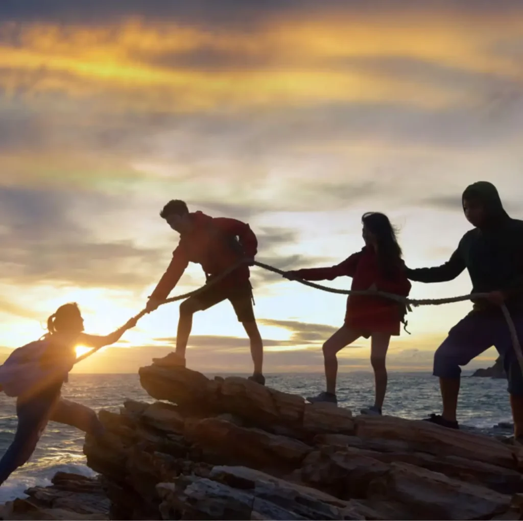 a team of people pulling a woman up some rocks with a rope Image